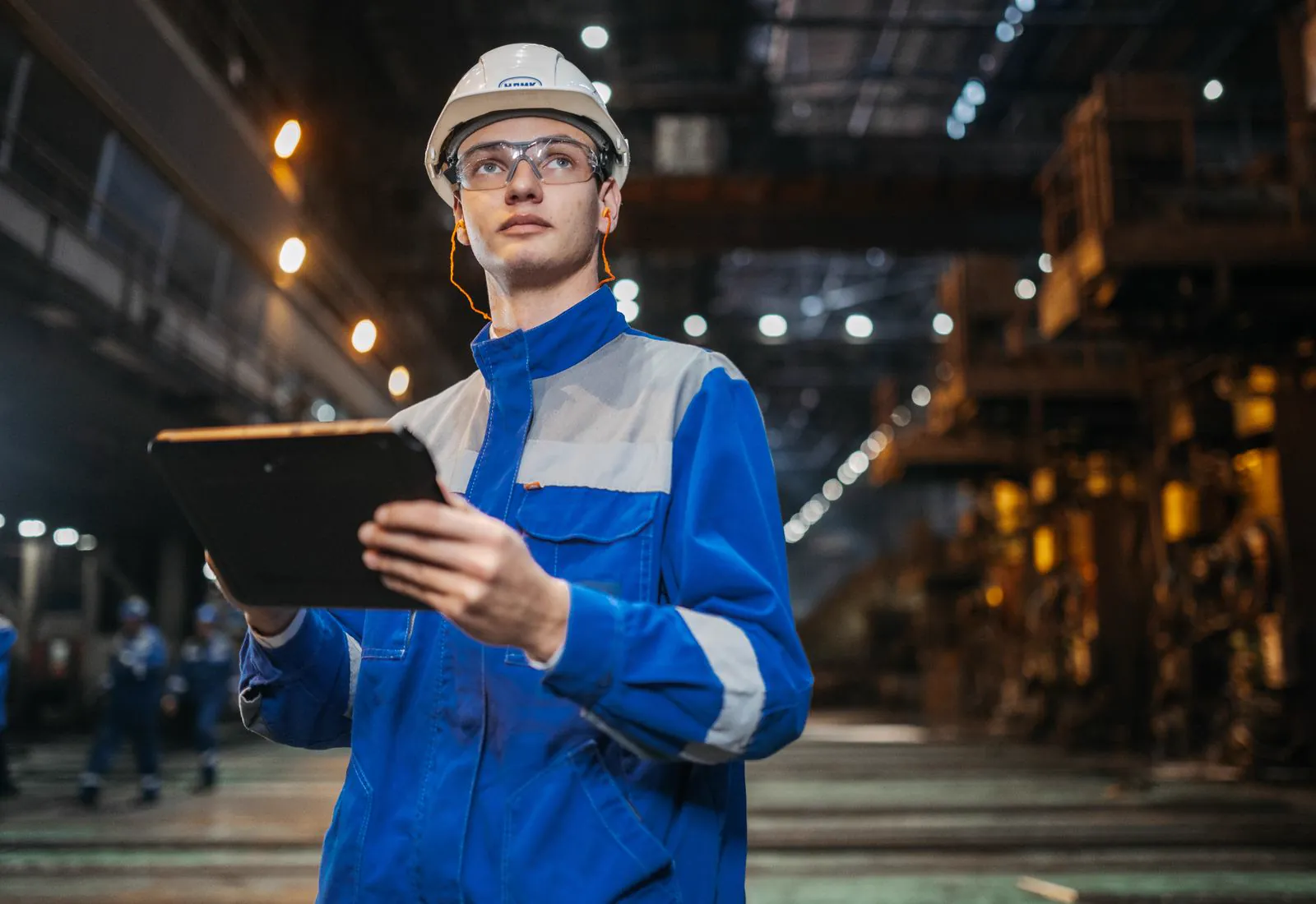 Engineer in safety gear using a tablet on a factory floor